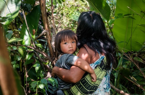 Mujer indígena ka'apor entre la vegetación de la selva amazónica con su hijo en brazos