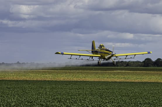 Un avión de hélice rocía un campo de soja con pesticidas desde el aire