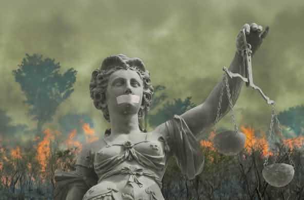 Fotomontaje: Una estatua de la Justicia con la boca tapada ante la selva tropical en llamas
