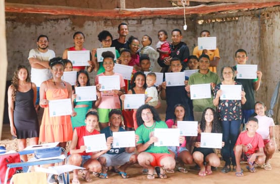31 personas jóvenes y niños, de pie y cuclillas, en una sala sosteniendo los diplomas obtenidos tras haber completado un taller de comunicación