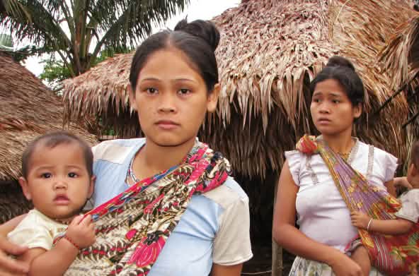 Dos mujeres con sus bebés frente a las casas de su comunidad