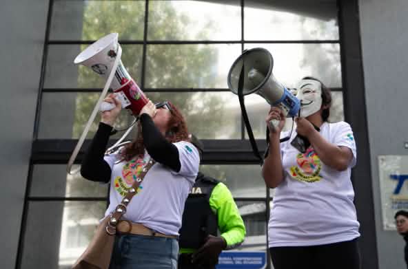 Dos miembros del colectivo ecuatoriano YASunidos protestan con megáfonos frente a la sede del Tribunal Contencioso Electoral (TCE)