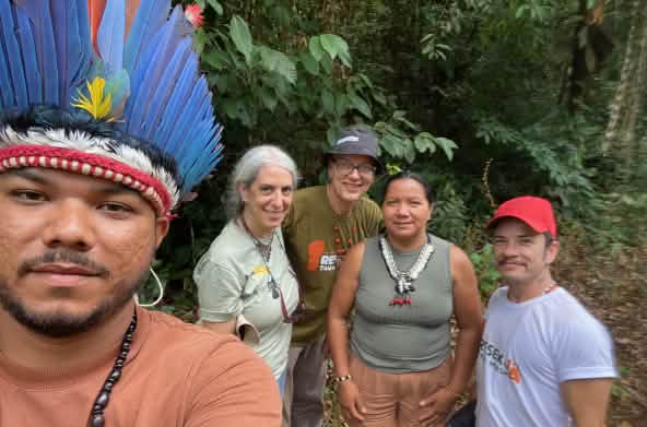 Selfie de un indígena con corona de plumas, situado a la izquierda de la imagen, junto a tres miembros de Salva la Selva y la cacica indígena Miriam Tembé. Se encuentran ante la vegetación de la selva en el estado amazónico de Pará.