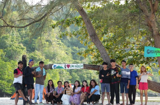Un grupo de jóvenes sentados y de pie frente a un árbol en la playa en defensa de la naturaleza