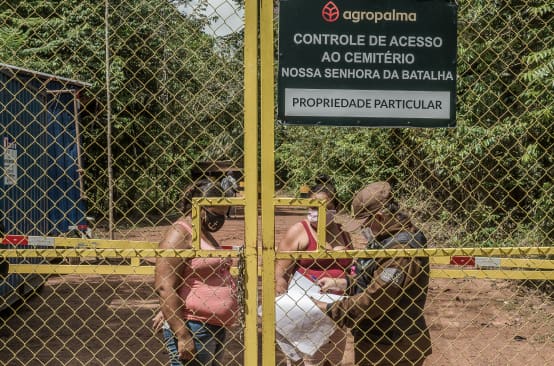 Para acudir al cementerio comunitario, dos mujeres se ven obligadas a pasar por un punto de control de la empresa Agropalma. En el cartel de la empresa se lee: “Agropalma. Control de acceso al cementerio de Nossa Senhora da Batalha. Propiedad privada"