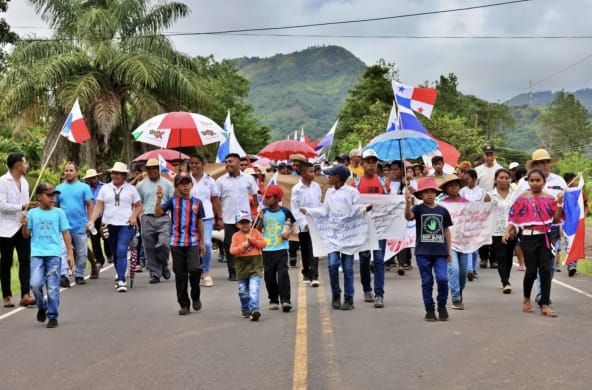 Manifestantes marchan con pancartas, banderas nacionales y paraguas por una carretera en Panamá
