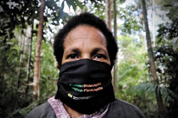 Mujer papú con tapabocas en el que se lee "Protege el bosque - el bosque nos protege"