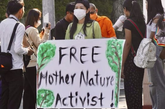 Joven mujer con un gran cartel en el que se lee «¡Liberad a los activistas de Mother Nature!».
