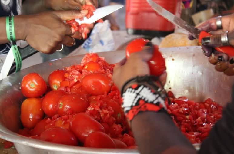 Detalle de las manos de dos personas cortando tomates en una fuente de metal