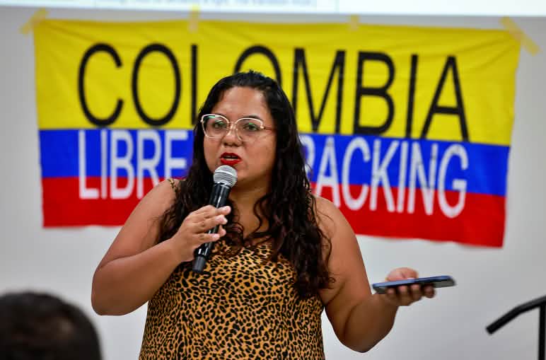Participante de la Cumbre de los Pueblos más allá de los Combustibles Fósiles, con pancarta detrás en la que se lee "Colombia libre de fracking"