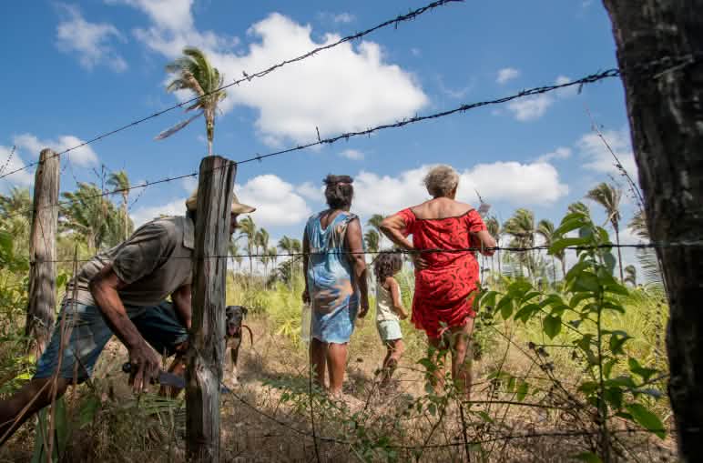 Hombre pasando por debajo de un alambre de púas, detrás del cual se encuentran las mujeres que ya pasaron