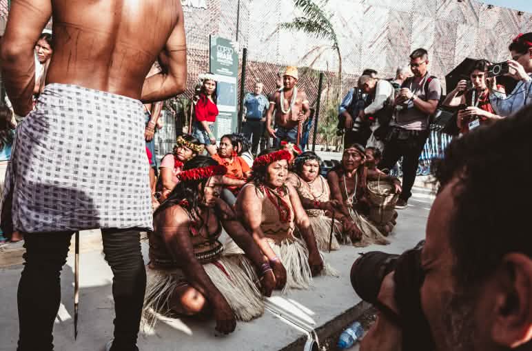 Mujeres indígenas Munduruku sentadas en el suelo bloqueando la entrada de la COP30