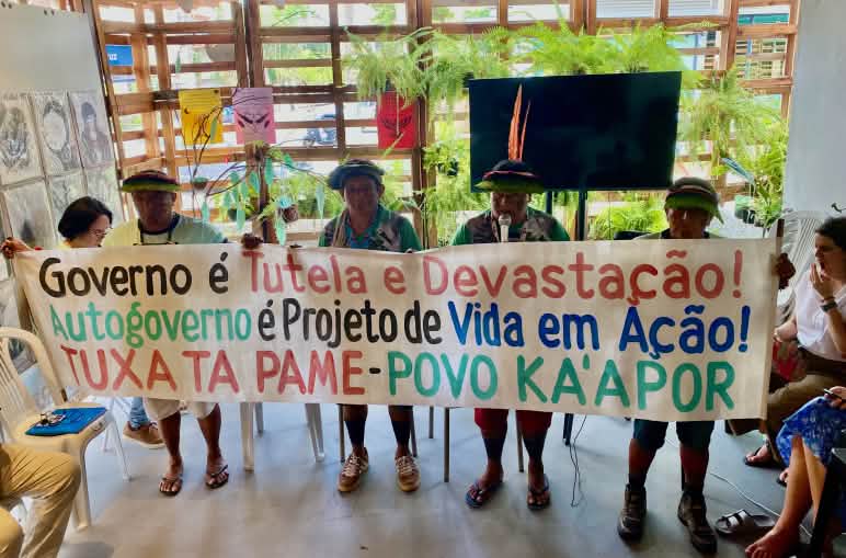 Cuatro indígenas Ka’apor sostienen una pancarta en la que se lee “Gobierno es tutela y devastacion. Autogobierno es proyecto de vida en Acción”