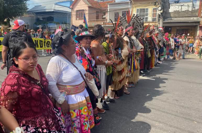 Mujeres y hombres indígenas con vestimentas coloridas formando una línea durante la manifestación global por el clima en las calles de Belém do Pará