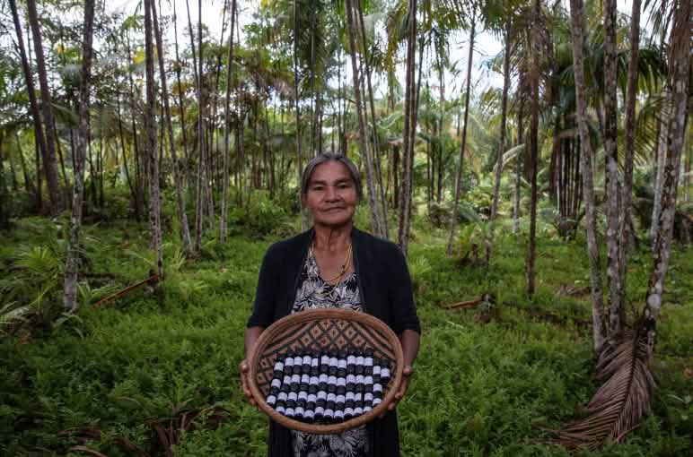 Una mujer indígena muestra una cesta llena de pequeños envases de aceites esenciales