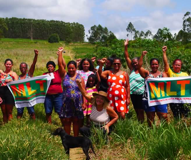 Un grupo de 15 mujeres protesta con los puños en alto y dos pancartas en las que se lee MLT Movimento de Luta pela Terra