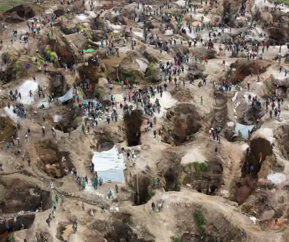 Vista aérea de una mina, con agujeros profundos, parcialmente llenos de agua, entre los cuales se encuentran numerosas personas