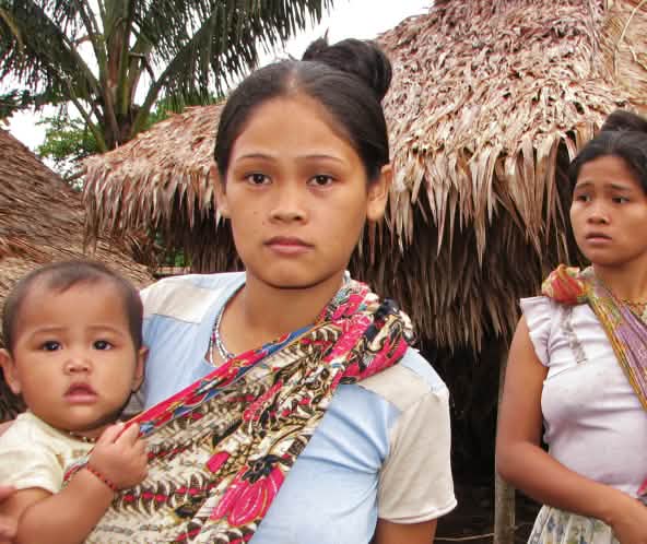 Dos mujeres con sus bebés frente a las casas de su comunidad