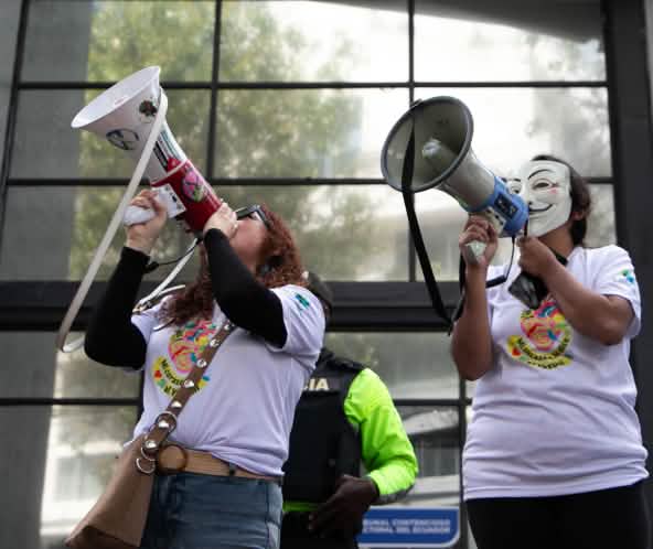Dos miembros del colectivo ecuatoriano YASunidos protestan con megáfonos frente a la sede del Tribunal Contencioso Electoral (TCE)