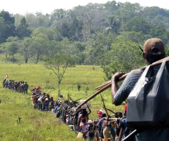 Indígenas en fila atraviesan una sabana para ir a cazar