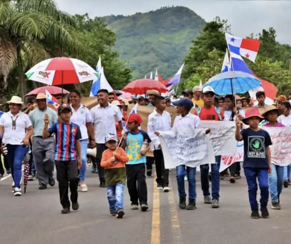 Manifestantes marchan con pancartas, banderas nacionales y paraguas por una carretera en Panamá