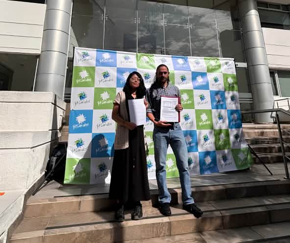 Una mujer y un hombre frente a un fotocall del colectivo YASunidos, delante de un edificio con documentos en la mano