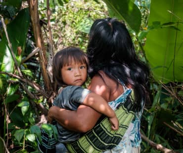 Mujer indígena ka'apor entre la vegetación de la selva amazónica con su hijo en brazos