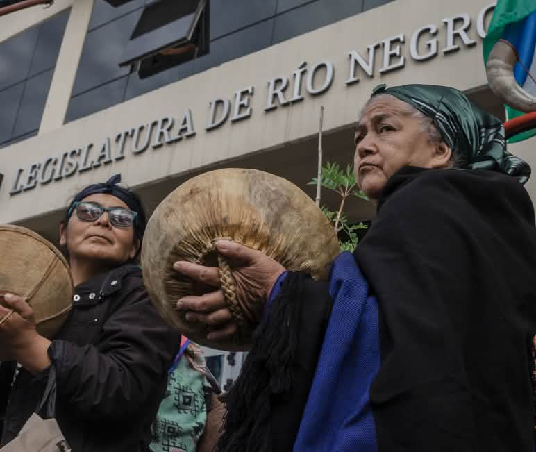 Dos mujeres Mapuche durante una protesta ante la Legislatura de la provincia de Río Negro en diciembre 2023 Dos mujeres Mapuche en protesta ante la legislatura (parlamento) de la provincia de Rio Negro, Argentina, contra las modificaciones a la Ley de tierras fiscales, y su uso extractivo, minero e inmobiliario entre otras medidas
