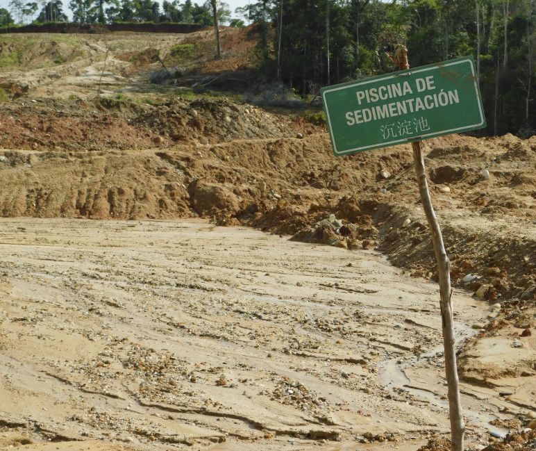 Así queda el paisaje sustituido por las actividades mineras Paisaje devastado debido a la presencia de piscinas de sedimentación, en las que se ve un cartel que contiene letras en español y en chino.
