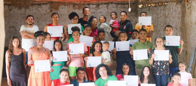 31 personas jóvenes y niños, de pie y cuclillas, en una sala sosteniendo los diplomas obtenidos tras haber completado un taller de comunicación