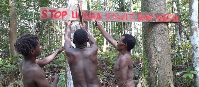 Tres indígenas papúes con un cartel en defensa de su bosque