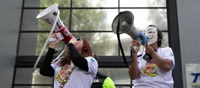 Dos miembros del colectivo ecuatoriano YASunidos protestan con megáfonos frente a la sede del Tribunal Contencioso Electoral (TCE)