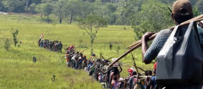 Indígenas en fila atraviesan una sabana para ir a cazar