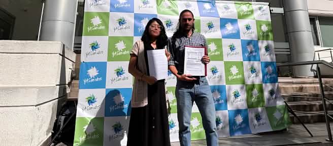 Una mujer y un hombre frente a un fotocall del colectivo YASunidos, delante de un edificio con documentos en la mano