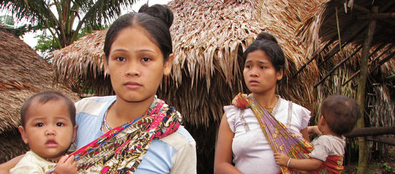 Dos mujeres con sus bebés frente a las casas de su comunidad