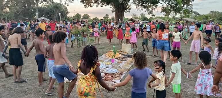 Decenas de personas, entre mujeres, hombres, niños y ancianos, forman un círculo alrededor de una ofrenda extendida en el suelo con alimentos, semillas y otros productos de la tierra (ändern).