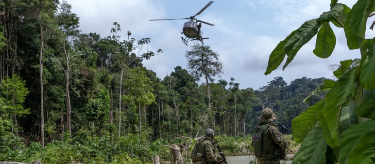 Dos agentes armados de la agencia ambiental IBAMA, vestidos con trajes de camuflaje, bajo un helicóptero durante en una operación de contra la minería ilegal de oro en la selva tropical amazónica
