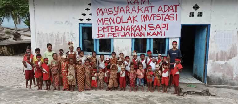 Grupo de niños delante de una escuela en la que cuelga una pancarta con un mensaje en indonesio