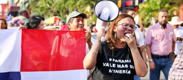 Una mujer se manifiesta en contra de la minería de cobre en Panamá, con una camiseta con la leyenda "#Panamá vale más sin minería". Al fondo la bandera panameña.