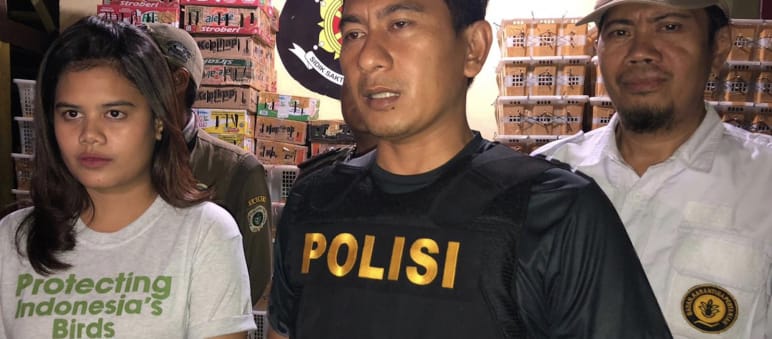 Una joven con una camiseta de FLIGHT y un policía en un almacén lleno de cajas de aves