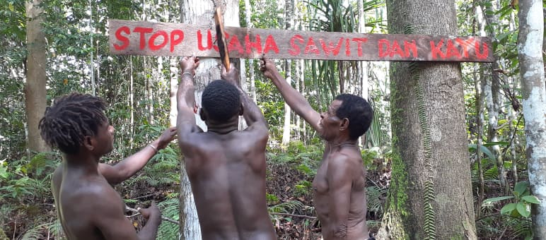 Tres indígenas papúes con un cartel en defensa de su bosque