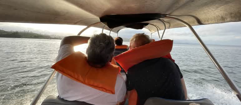 Personas con salvavidas en una embarcación navegando con el sol del amanecer de frente