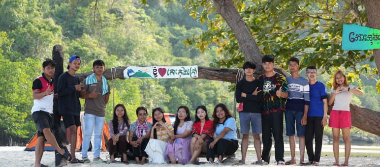 Un grupo de jóvenes sentados y de pie frente a un árbol en la playa en defensa de la naturaleza