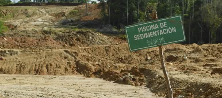 Paisaje devastado debido a la presencia de piscinas de sedimentación, en las que se ve un cartel que contiene letras en español y en chino.