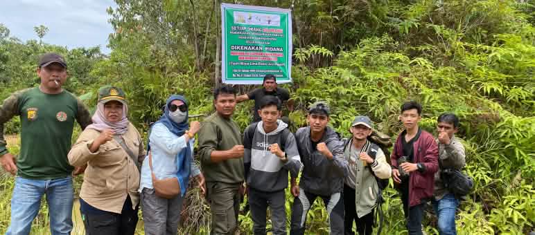 Un grupo de personas frente a un cartel que advierte sobre las fuertes sanciones por cualquier actividad prohibida en el bosque