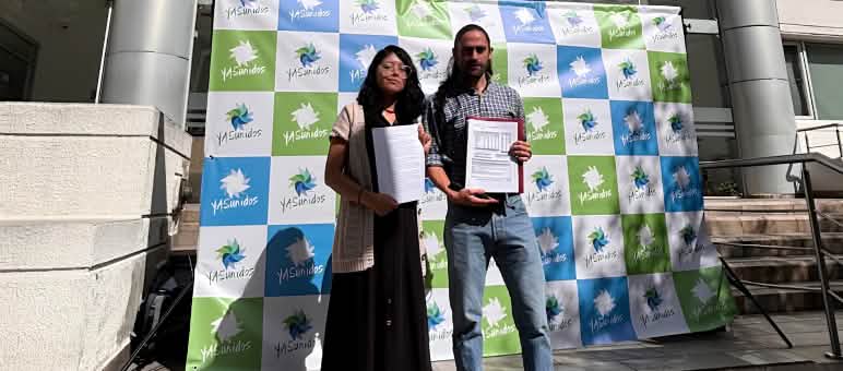 Una mujer y un hombre frente a un fotocall del colectivo YASunidos, delante de un edificio con documentos en la mano