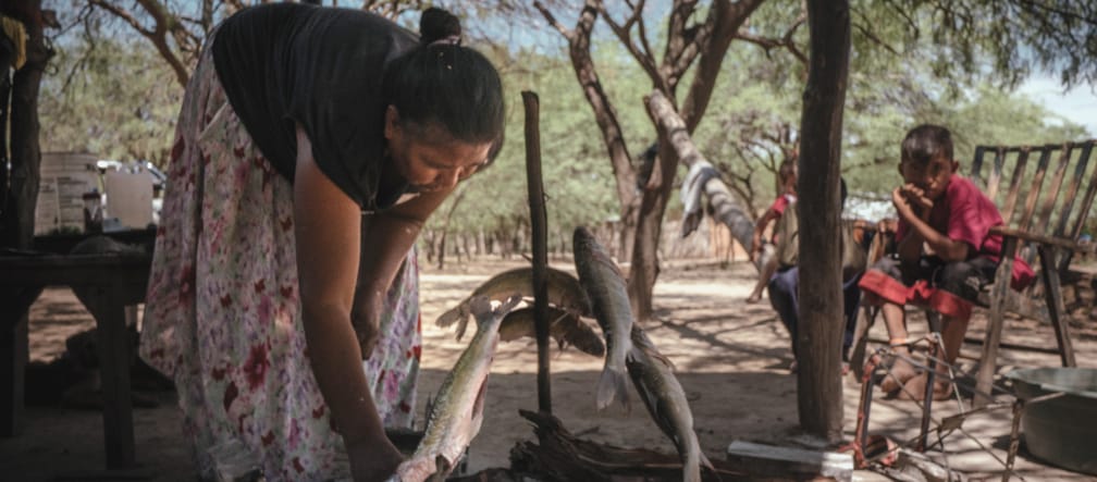Mujer asando pescado bajo la atenta mirada de dos niños