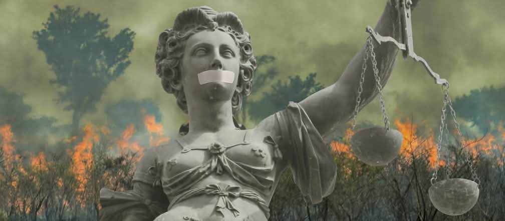 Fotomontaje: Una estatua de la Justicia con la boca tapada ante la selva tropical en llamas