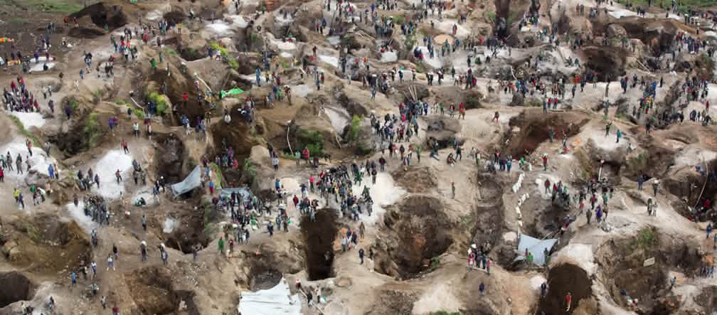 Vista aérea de una mina, con agujeros profundos, parcialmente llenos de agua, entre los cuales se encuentran numerosas personas