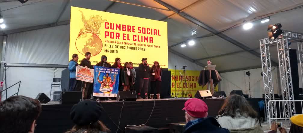 Plenaria de la cumbre social por el clima, organizada por la sociedad civil en Madrid, en la COP25 Cumbre social por el clima paralela a la COP25, en diciembre 2019 Madrid. Un grupo de personas sostienen pancartas sobre un escenario.